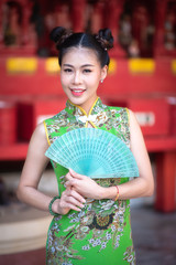 A beautiful woman wearing a green cheongsam is standing, holding a fan in cheongsam and in the Chinese New Year