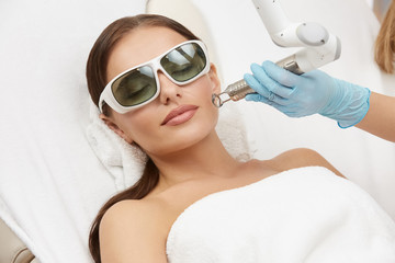 attractive woman receiving face treatment on her cheek with laser in glasses