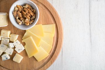 Delicious cheese plate with cheeses Dorblu, Brie, Camembert, nuts. Serving on a wooden round board. Healthy snack or aperitif for white or red wine. Selective focus, close-up