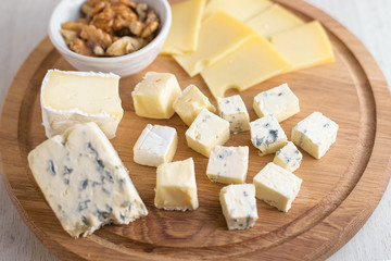 Delicious cheese plate with cheeses Dorblu, Brie, Camembert, nuts. Serving on a wooden round board....