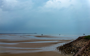 Ocean shore view at low tide on a rainy day, sand, water spills. Travel by China and world
