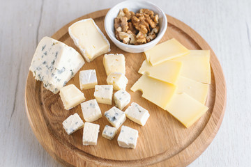Delicious cheese plate with cheeses Dorblu, Brie, Camembert, nuts. Serving on a wooden round board. Healthy snack or aperitif for white or red wine. Selective focus, close-up