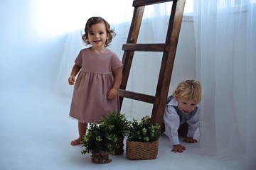 Little boy and girl are playing with plants near the wooden stairs in a bright room.