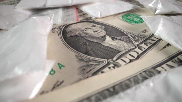 Dollar bills and white powder drugs in bags rotate in front of the camera