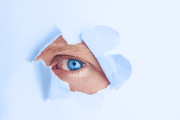 An eye of classic blue color looks through a hole in blue paper. The concept of secrecy, peeping. Minimalism, place for text. Trend color 2020.