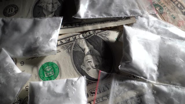 Dollar bills and white powder drugs in bags rotate in front of the camera