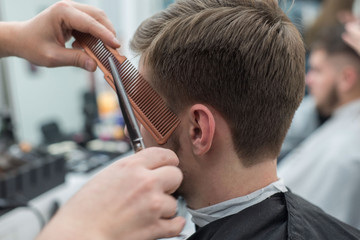 Master hairdresser cuts hair on the head of a young bearded guy. Close-up of the hand of a professional haircutter with scissors in a barber shop.