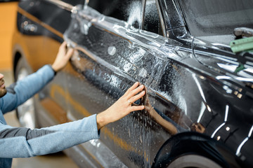 Car service worker sticking anti-gravel film on a car body for protection at the detailing vehicle workshop. Concept of car body protection with special films