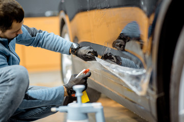 Car service worker splashing water on the car body, wetting it before anti-gravel film apply at the vehicle detailing service