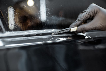 Worker trimming with cutter remains of a protective film, sticking it on a car body at the vehicle...