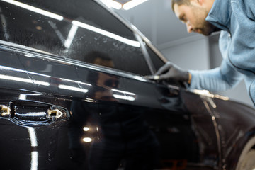 Worker trimming with cutter remains of a protective film, sticking it on a car body at the vehicle...