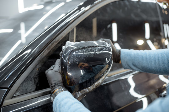 Man applying sticking protective film on a car mirror at the vehicle service station. Concept of car body protection with special films