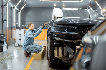 Man preparing protective film for sticking on a car body, marking it to with a pen at the vehicle...