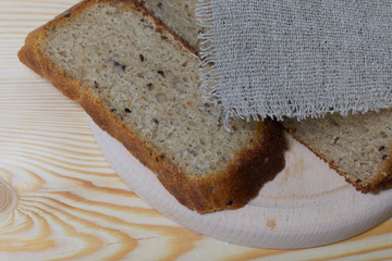 Freshly baked bread. A loaf of bread is cut and lies on a cutting board. It is covered with a piece of linen. Background from pine boards.