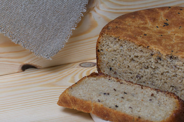 Freshly baked bread. A loaf of bread is cut and lies on a cutting board. It is covered with a piece of linen. Background from pine boards.