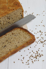 Freshly baked bread. A loaf of bread is cut and lies on a cutting board. Dill seeds are scattered nearby and a knife lies.