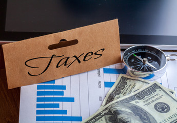 Taxes Words on tag with dollar note,smartphone,compass and graph on wood backgroud,Finance Concept