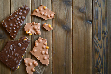 broken pieces of real Swiss lump chocolate with nuts on wooden background. space for text