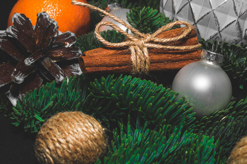 Close-up art installation for New Year or Christmas from spruce twigs, glass balls, cord balls, pine cone, one mandarin and cinnamon sticks.