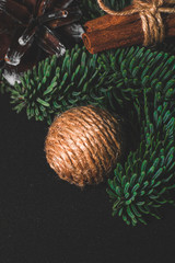 Close-up art installation on a black background for New Year or Christmas from spruce twigs,  cord balls, pine cone and cinnamon sticks.