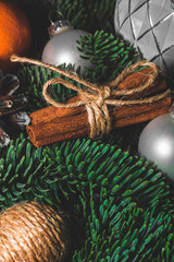 Close-up art installation for New Year or Christmas from spruce twigs, glass balls, cord balls, pine cone, one mandarin and cinnamon sticks.
