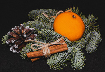 Art installation on a black background for New Year or Christmas from spruce twigs, pine cone, one mandarin and cinnamon sticks.