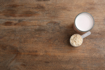 Protein shake and powder on wooden table, flat lay. Space for text