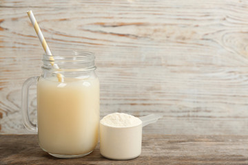 Protein shake and powder on wooden table, space for text