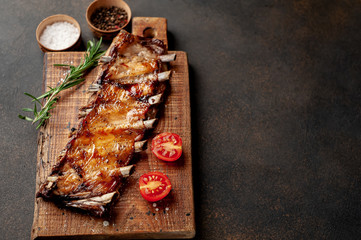 grilled pork ribs on a cutting board with spices on a stone background with copy space for your text