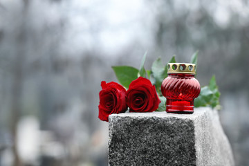 Red roses and candle on grey granite tombstone outdoors. Funeral ceremony