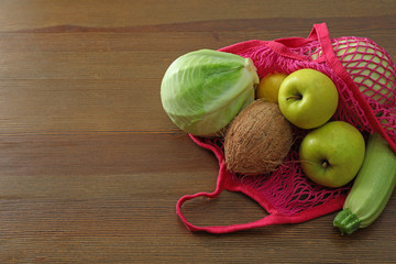 Net bag with vegetables and fruits on wooden table. Space for text