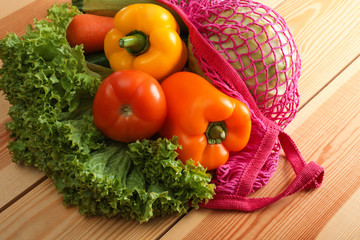 Net bag with vegetables on wooden table, closeup