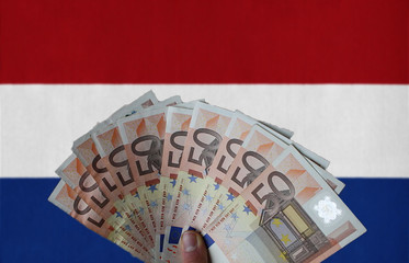The Netherlands flag with Euro banknotes in the hand