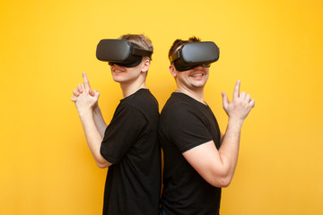 two guys in VR glasses on a yellow background, friends gamers in virtual reality glasses play a shooter and hold weapons