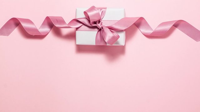 White gift box with a purple ribbon bow on pink background at the top. Flat lay top view stop motion animation with copyspace
