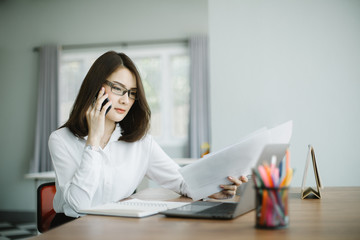 Beautiful young woman working on her laptop and talking phone in her office.