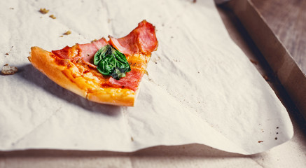 last one slice of Pizza with Mozzarella cheese, ham, bacon, Tomato sauce, pepper, Spices and basil. Italian pizza in cardboard box on wooden table background
