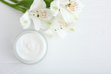 Fototapeta na wymiar Care cream and flowers on a light background top view. Skin care cosmetics.