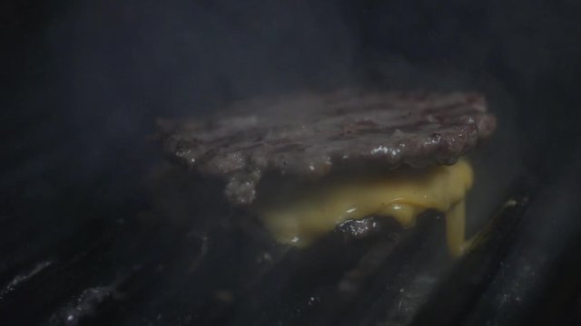 Meeting of grilled hamburger meat with cheddar cheese and rising smoke