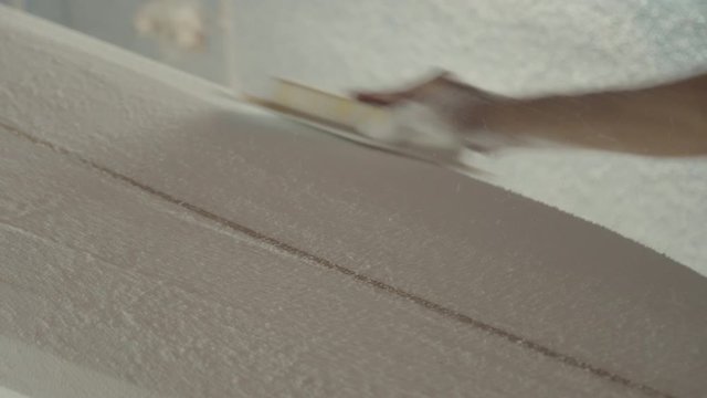 Sequence of shots of Indonesian surfboard shaper wearing protective equipment sanding surfboard lying on workbench with abrasive paper