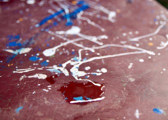 A close-up view of a wet drop on a red-painted stool with splashes of white and blue color
