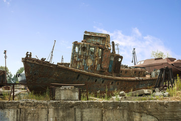 Fototapeta na wymiar An old abandoned rusty metal ship unfit for use lies on a pier on the river bank. An old unusable ship on the shore on concrete blocks.