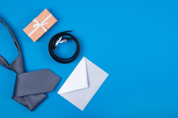 Composition of man's accessories grey silver neck tie, craft gift box, envelope and belt on blue cyan background. Top view. Man's fashionable style concept. Copy space.