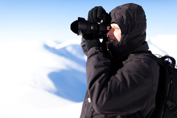 Fototapeta na wymiar Young man photographer in winter clothing standing and making photo in sunlight