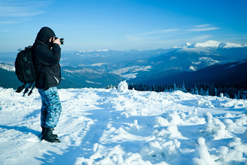 Fototapeta na wymiar Photographer standing with camera on hill with panoramic view of winter valley