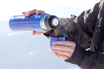 Naklejka premium Mans hands pouring fresh hot tea from thermos to cup