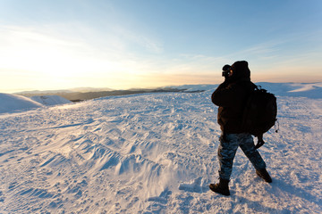 Young man photographer in winter clothing standing and making photo in sunlight