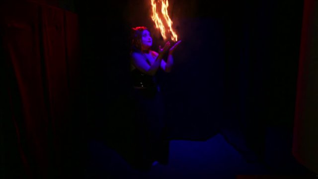 Woman devil dancing with fiery streams on her hands on a black background.