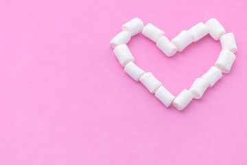 a shape of heart made of small marshmallows on a pink background