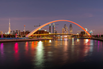 Fototapeta na wymiar Panoramic night view on Dubai at blue hour, showing Bridge of tolerance and iconic buildings and construction cranes